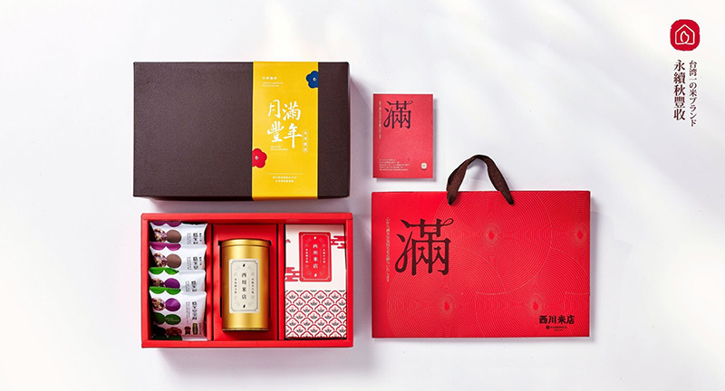 中秋禮盒組，在白色背景上，中秋禮盒內由右到左依序放著四包堅果酥、金色茶罐裝的紅茶與一包米香棒，旁邊搭配紅色手提紙袋與滿字賀卡。