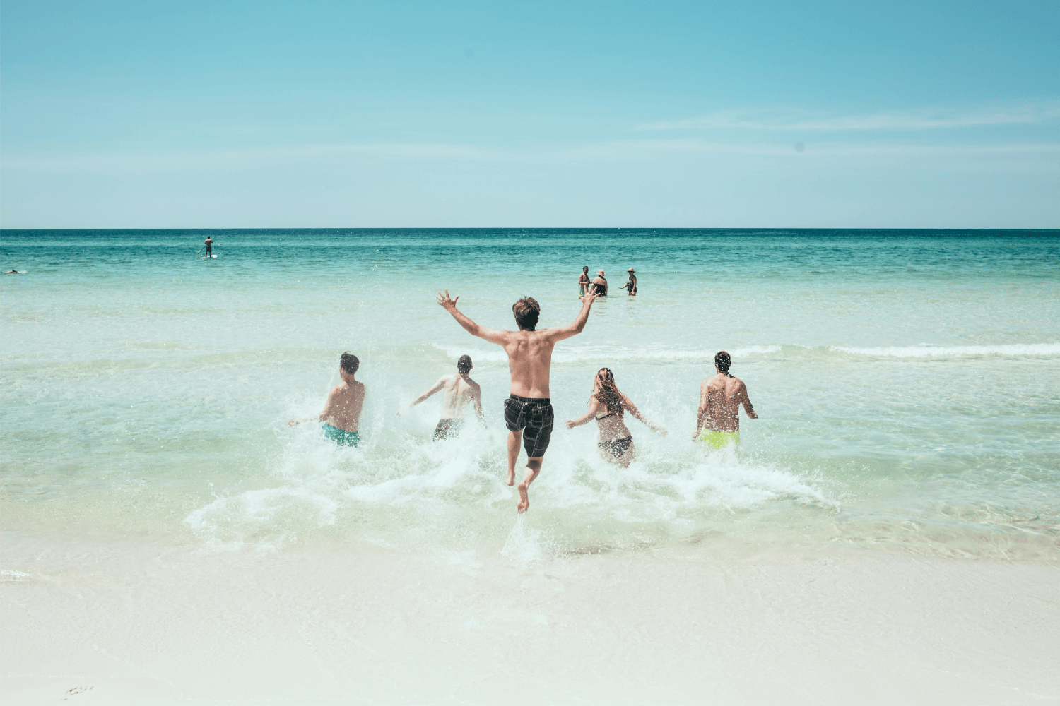 一群人在陽光下奔向大海，享受夏日海灘活動，象徵戶外玩水時防曬與肌膚保護的重要性