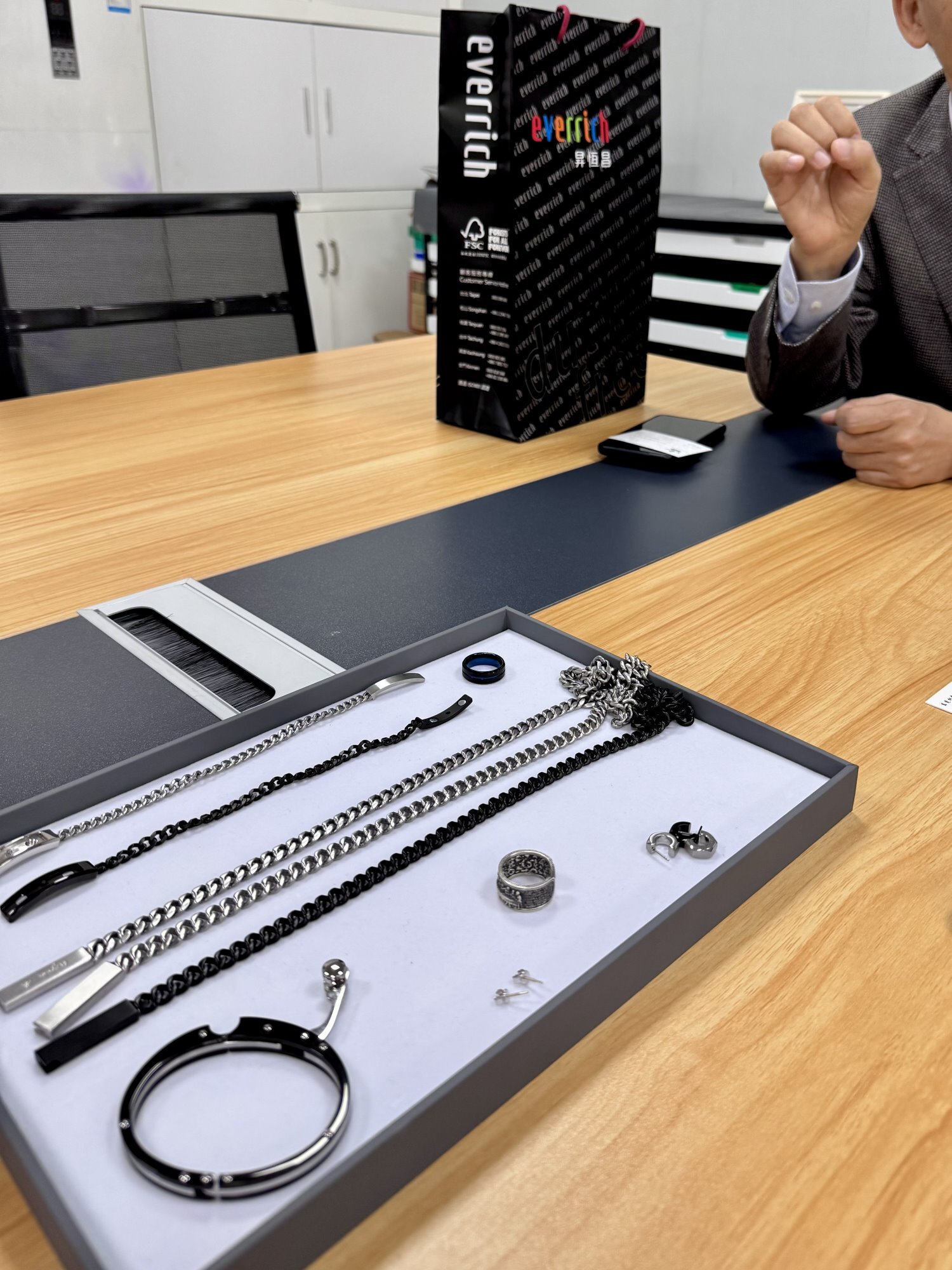 Set de joyería masculina sobre mesa de reunión: collar, pulsera, anillos y aretes en combinación negro y plata
