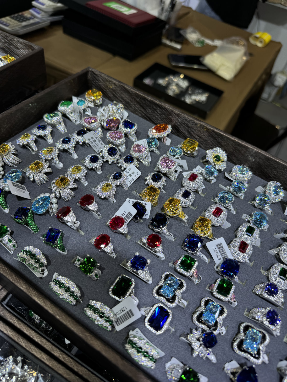 Bandeja con anillos de piedras de colores; monturas de plata con múltiples gemas, exhibidas en mercado mayorista de joyería