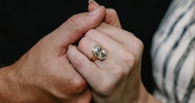 Close-up of Taylor Swift’s left hand, showing she is wearing a large old mine-cut diamond ring on her finger.
