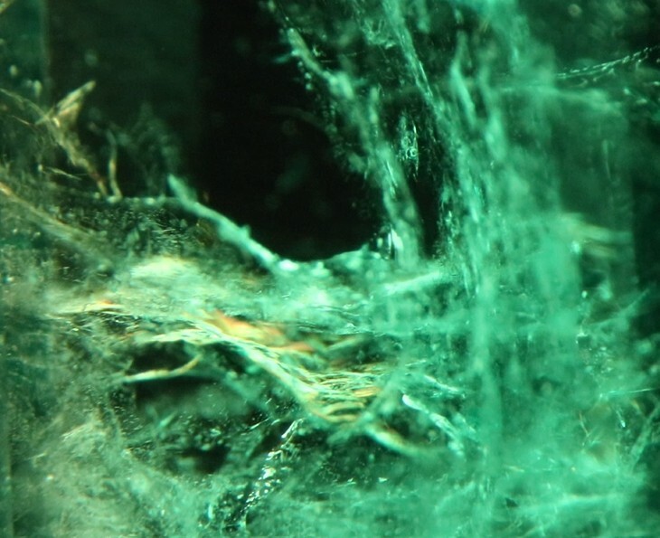 Microscopic view of a resin-filled emerald, showing internal fractures with distinctive yellow flash effect from the filling.