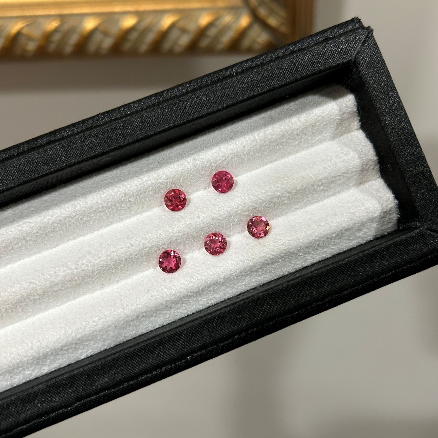 A set of round-cut rubellite gemstones displayed in a black jewelry box.