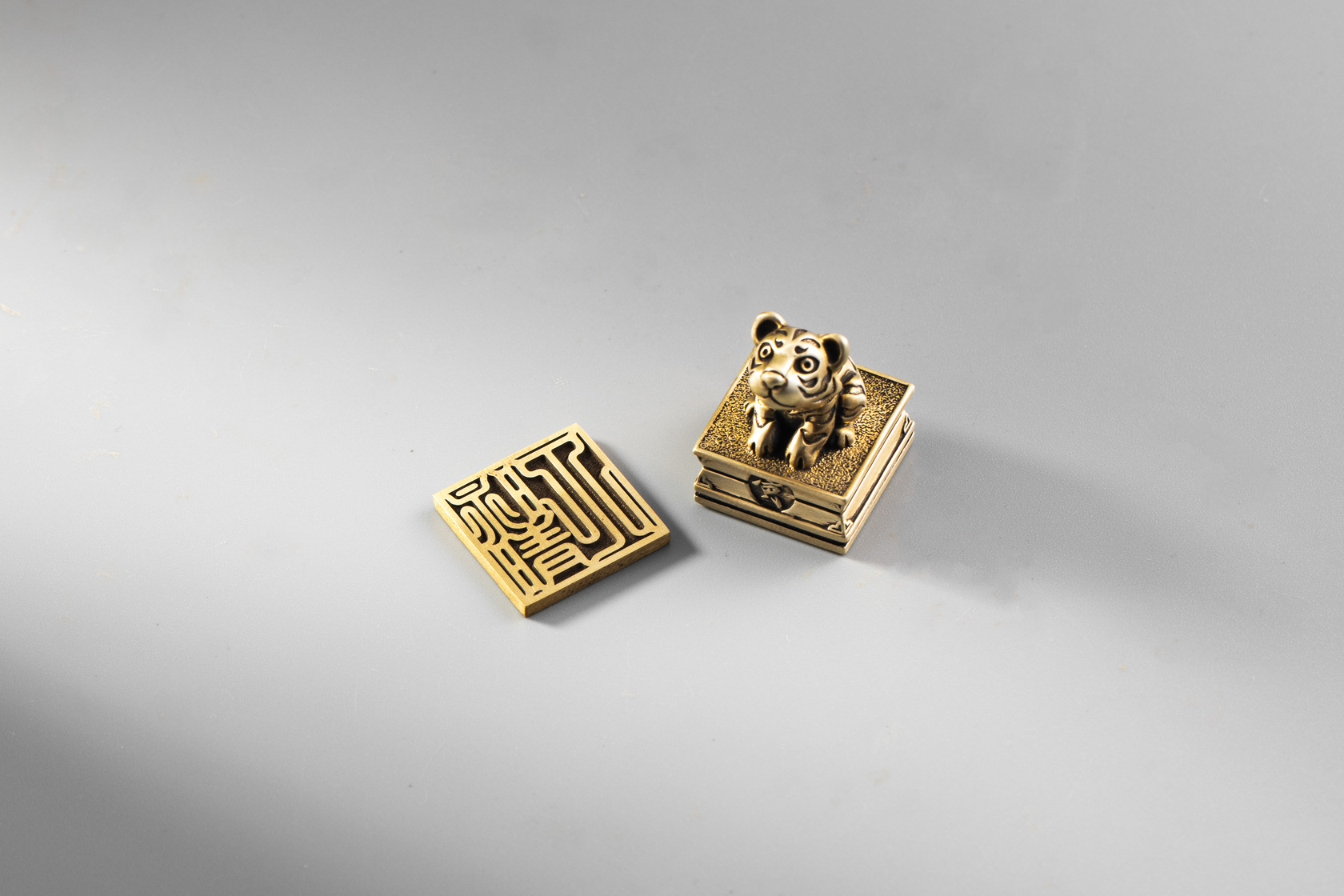 JK銀飾金屬印章古印篆字體展示；方形印面近拍，線條圓轉帶金石味，十二生肖的老虎造型印章，整體為黃銅霧金色調。