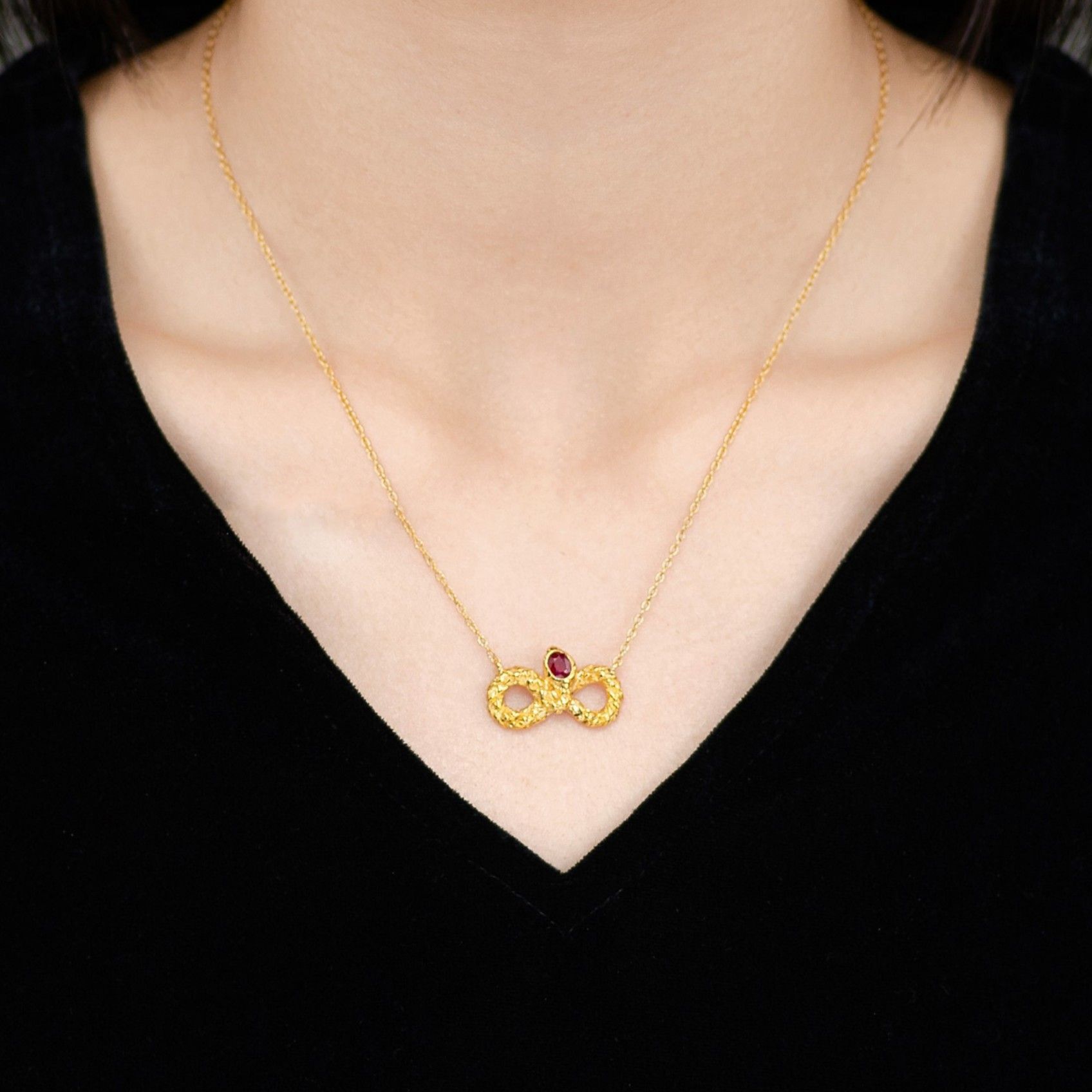 Close-up of a woman wearing a Victorian-style gold necklace featuring a snake-shaped pendant adorned with a red ruby at the center.