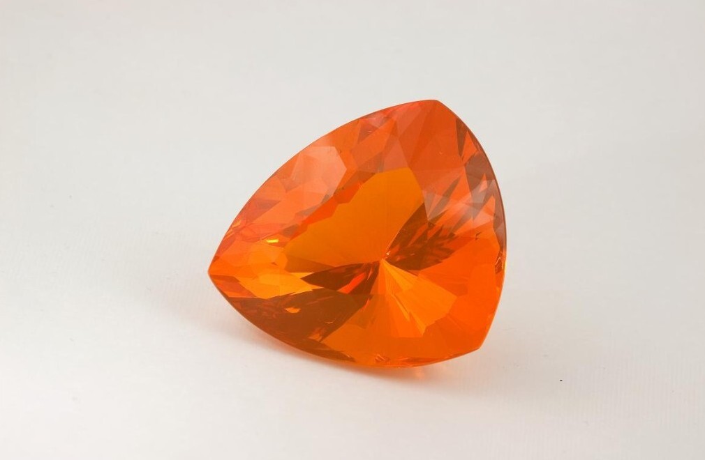 A Brazil fire opal with a vivid orange hue and trilliant cut, displaying bright internal reflections.