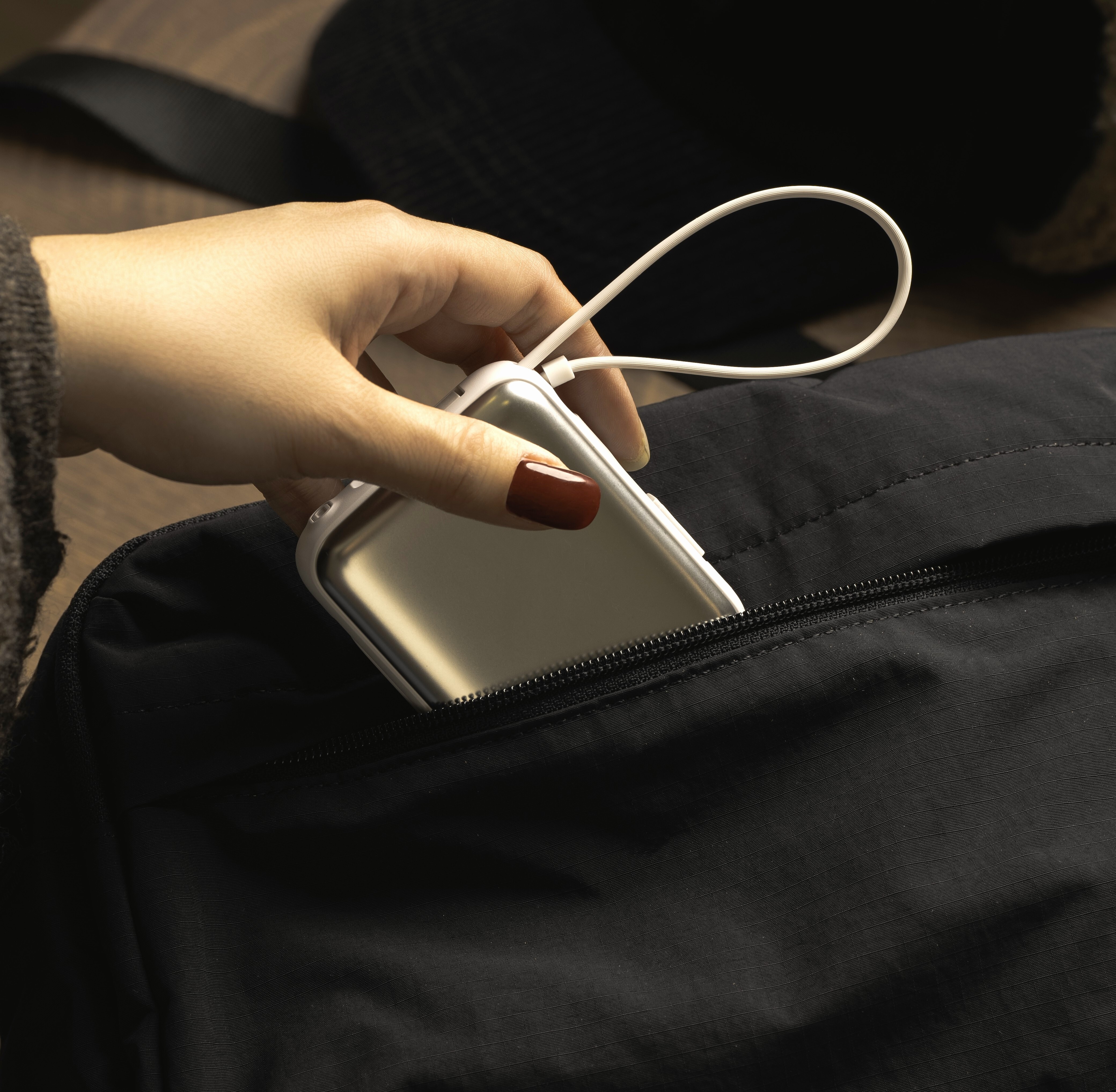 Champagne gold iWALK power bank being slipped into a black backpack pocket