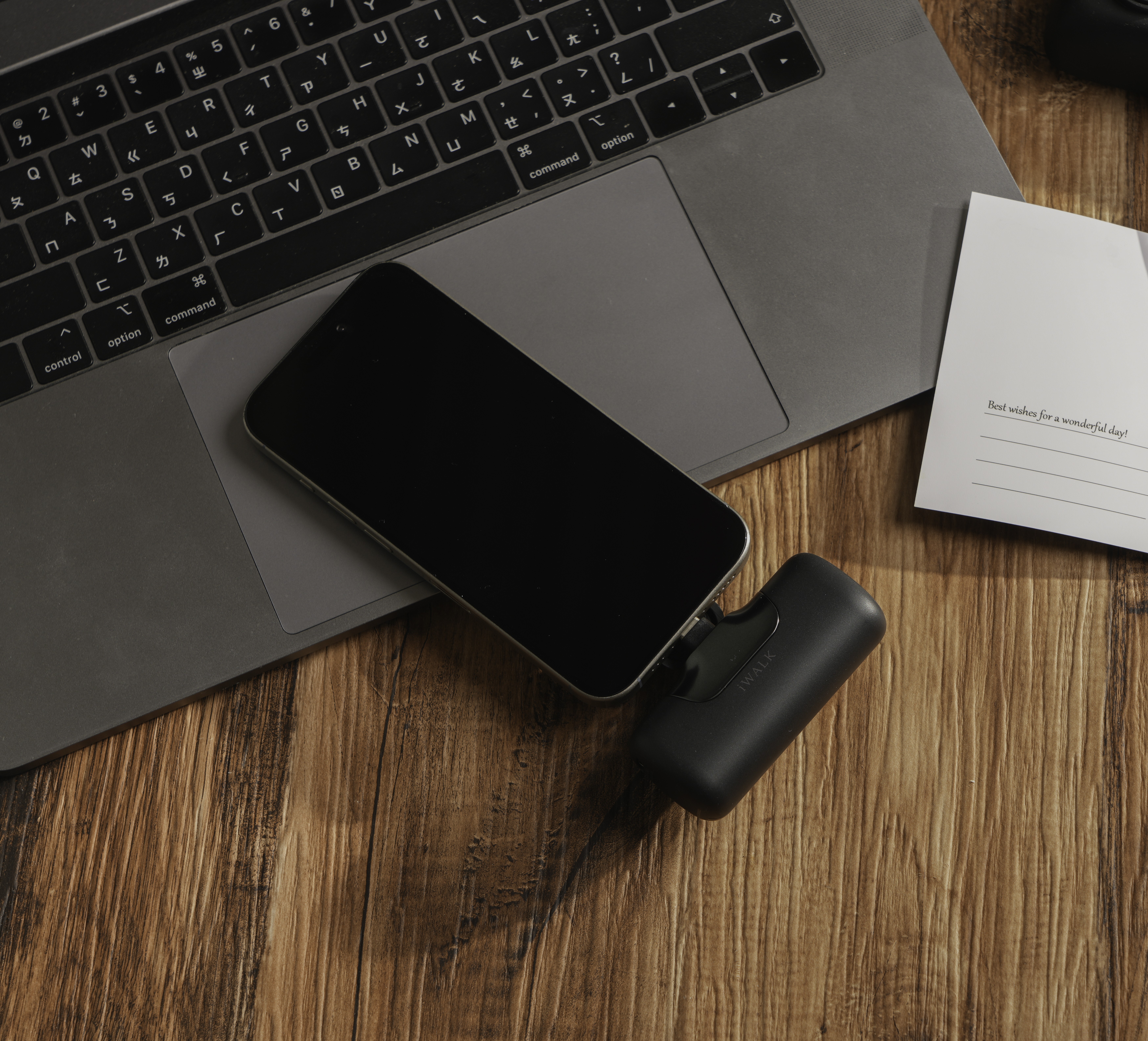 Black iWALK pocket power bank plugged into a phone on a wooden desk