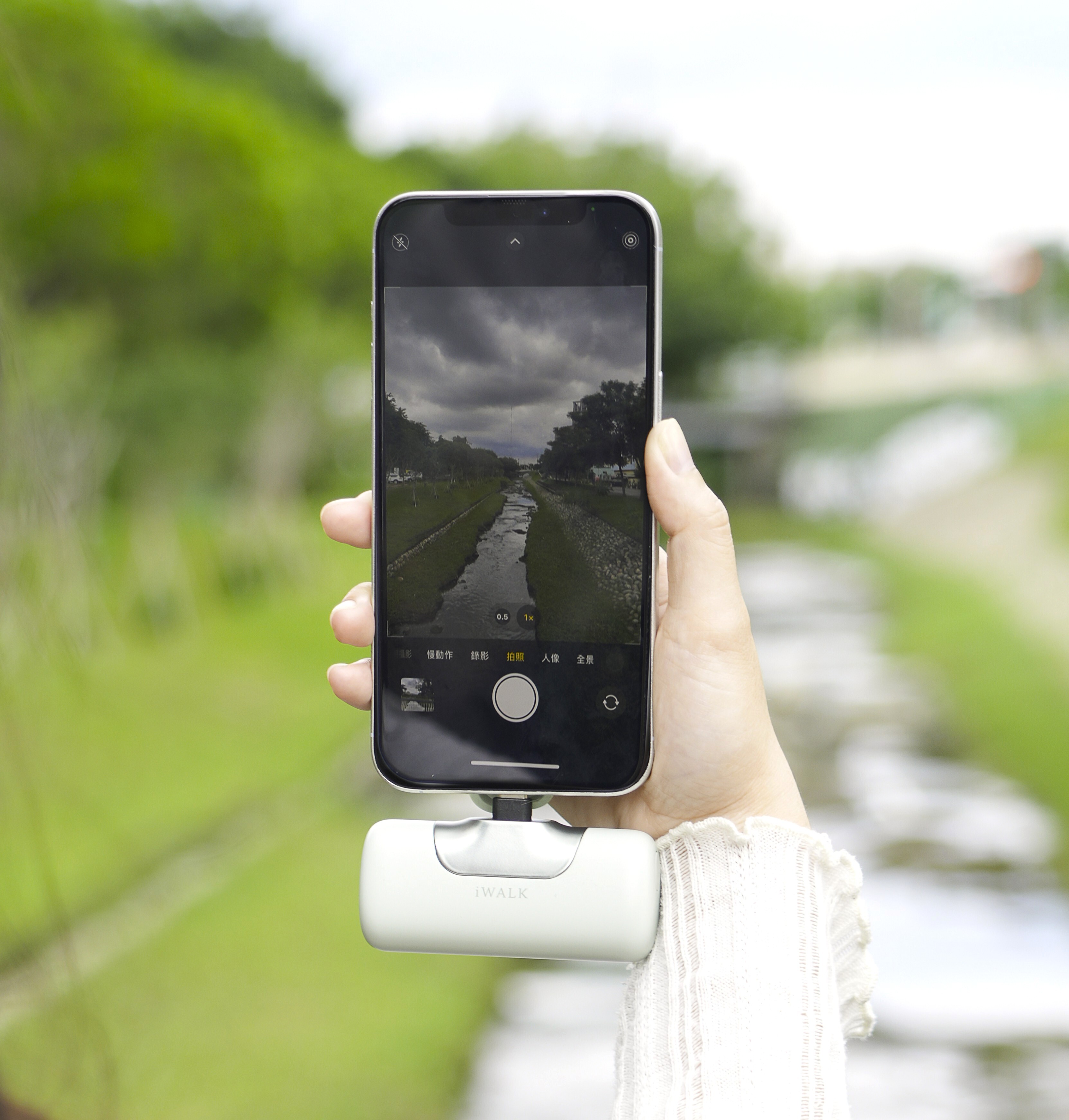 Taking a photo outdoors with a white iWALK pocket power bank plugged into the phone