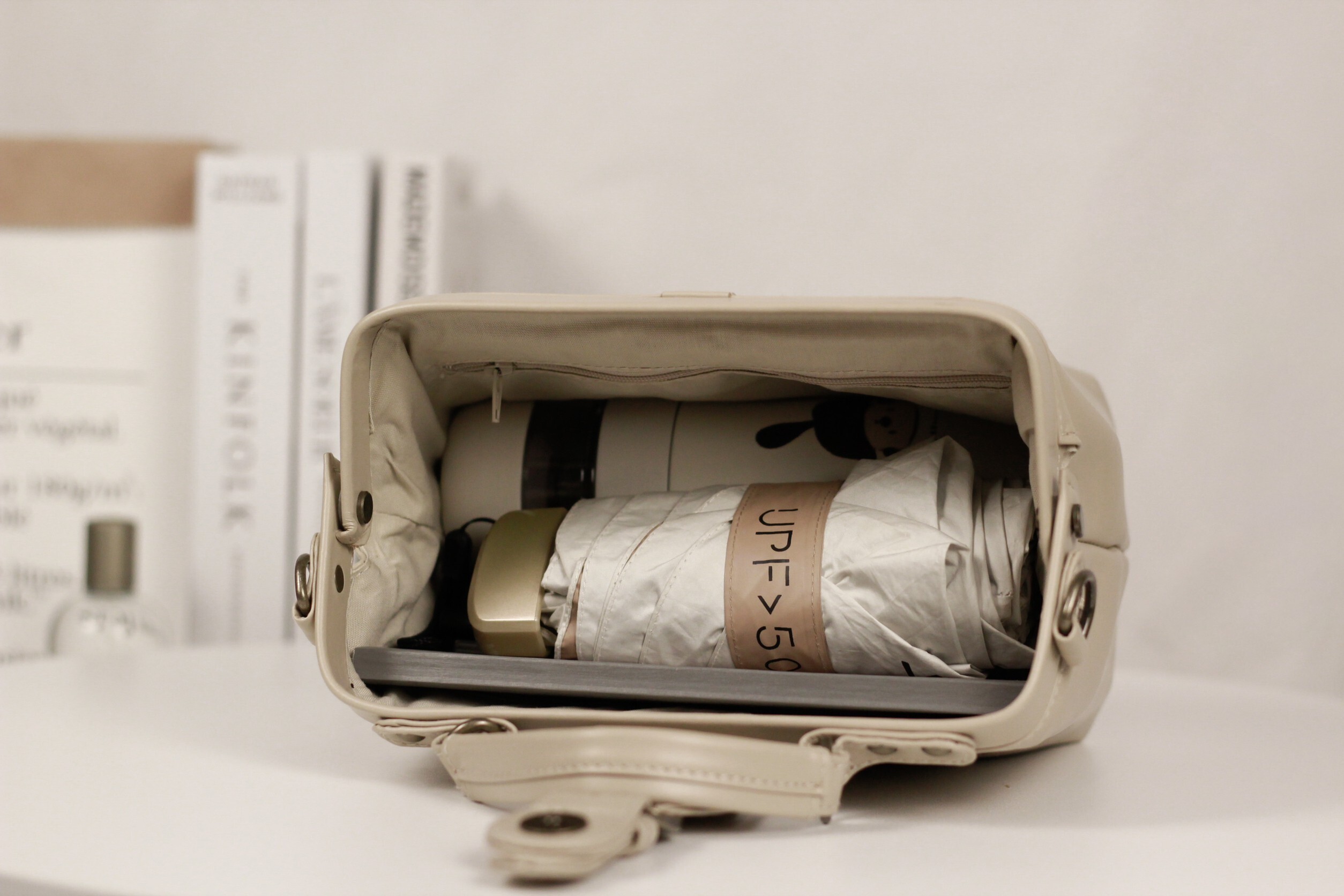 奶油杏白 Trista 醫生包超大口金開口展示,可見內部夾層長夾、摺疊傘及拉鍊袋細節