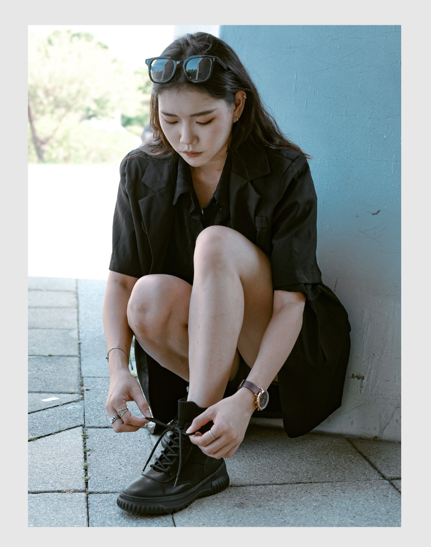 Sanly Joy 克洛伊厚底真皮短靴經典黑穿搭照。模特蹲下繫鞋帶的瞬間自然率真,展現生活感氛圍。鞋面真皮結合彈性襪筒設計,穿著柔軟不磨腳。5cm厚底修飾腿型比例,兼具舒適與時尚感,適合日常通勤、出遊及街頭風穿搭。