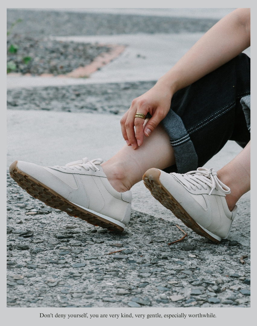 Sanly Joy 伊登復古休閒鞋燕麥奶霜色穿搭特寫照。模特自然坐姿展示鞋款側面與鞋底紋理，柔霧奶霜色鞋面結合復古橡膠底，展現輕盈舒適的日常感。