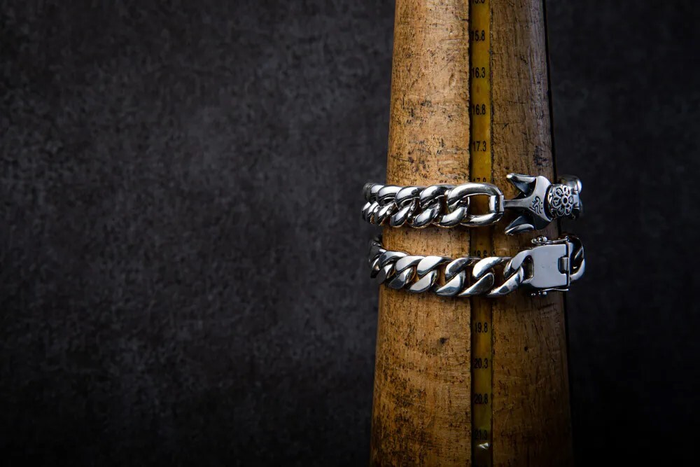 兩條相同鍊長的純銀古巴鍊手鍊繞在木製圓錐尺上，因鏈節厚度與扣頭結構不同，實際手圍貼合度產生差異之示意｜JK銀飾。