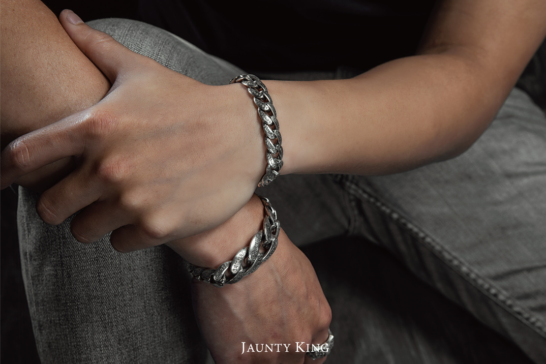 JK銀飾 925純銀「六字雕花」古巴鍊手鍊穿搭示意：男性手腕交握，雙圈疊戴展示，鏈節浮雕花紋與金屬光澤細節，厚實份量感，適合男士日常配戴。