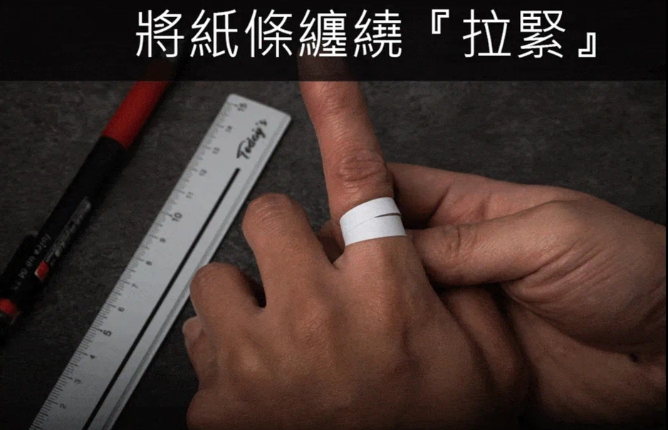 紙條量戒圍步驟示意：將無彈性紙條貼合繞在指根並「拉緊」，交會處做記號；旁置直尺與筆，稍後攤平量長換算美規戒圍。