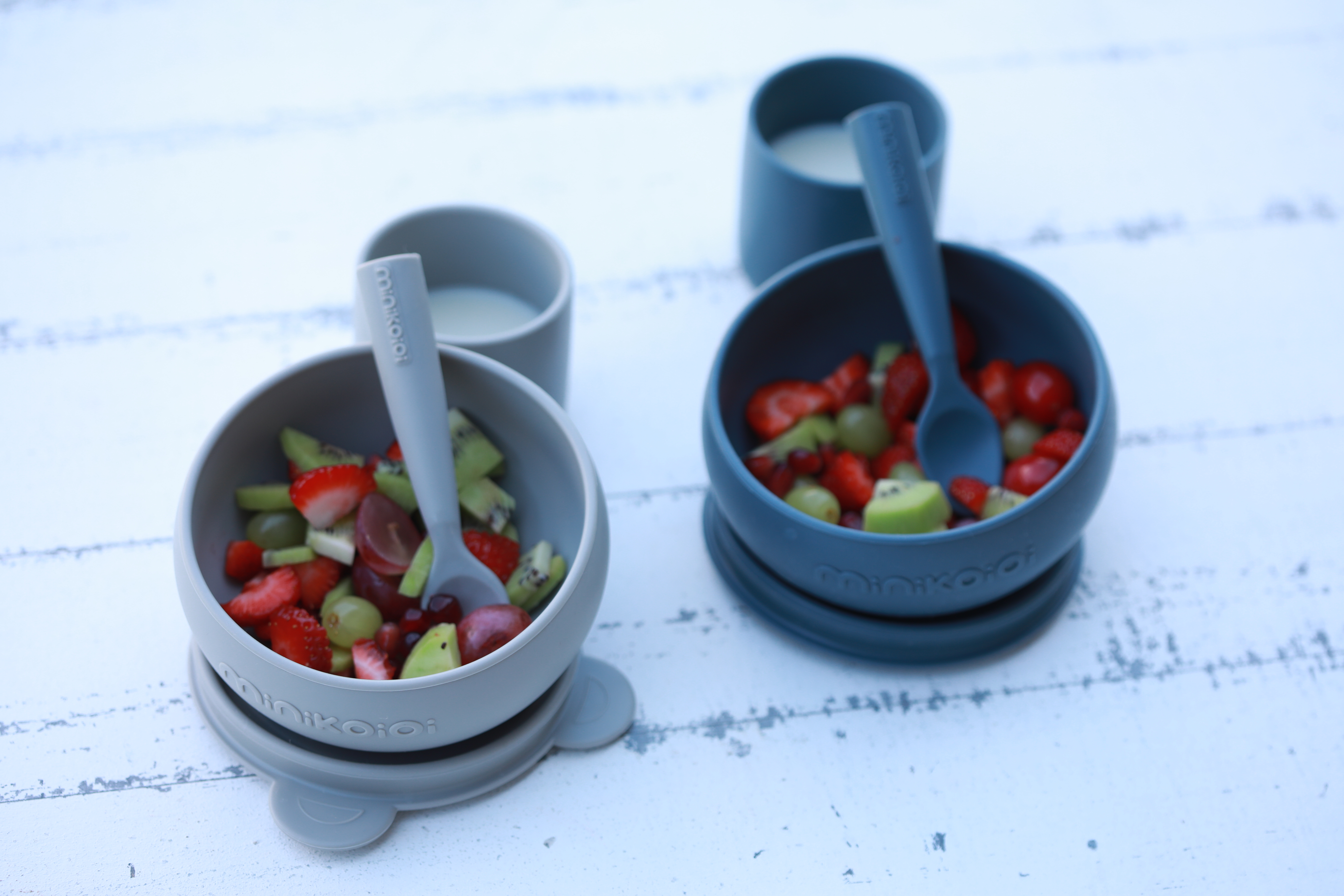兩個裝有水果的 minikoioi 矽膠吸盤碗，碗內有湯匙，背景有兩個小杯子，展示矽膠餐具的色彩與功能。