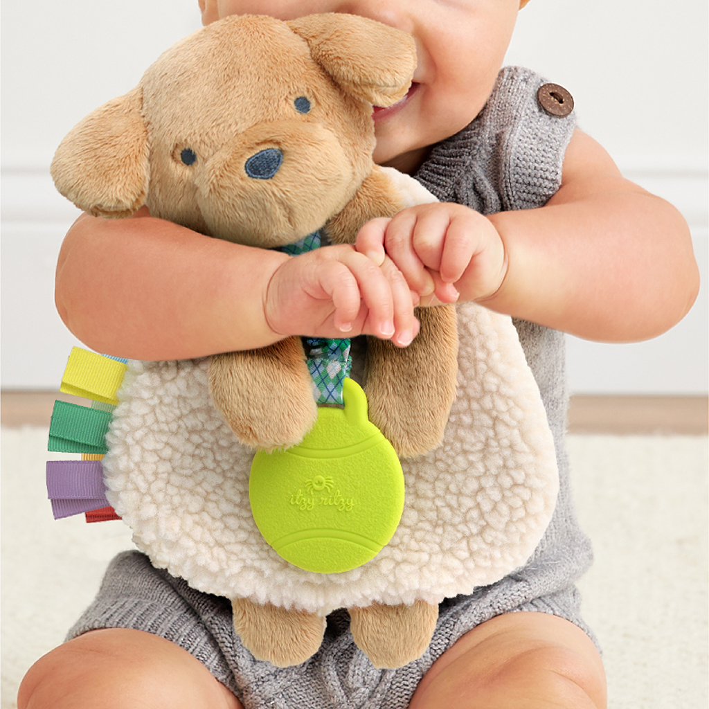 一位穿著灰色連身衣的寶寶緊緊抱著一隻棕色小狗造型的 Itzy Ritzy 咬咬安撫巾。 美國Itzy Ritzy 咬咬安撫巾：