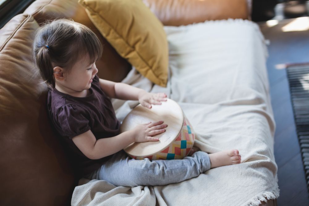 一個孩子正在玩泰國 Plantoys 木作兒童樂器-木箱鼓，敲打出節奏。