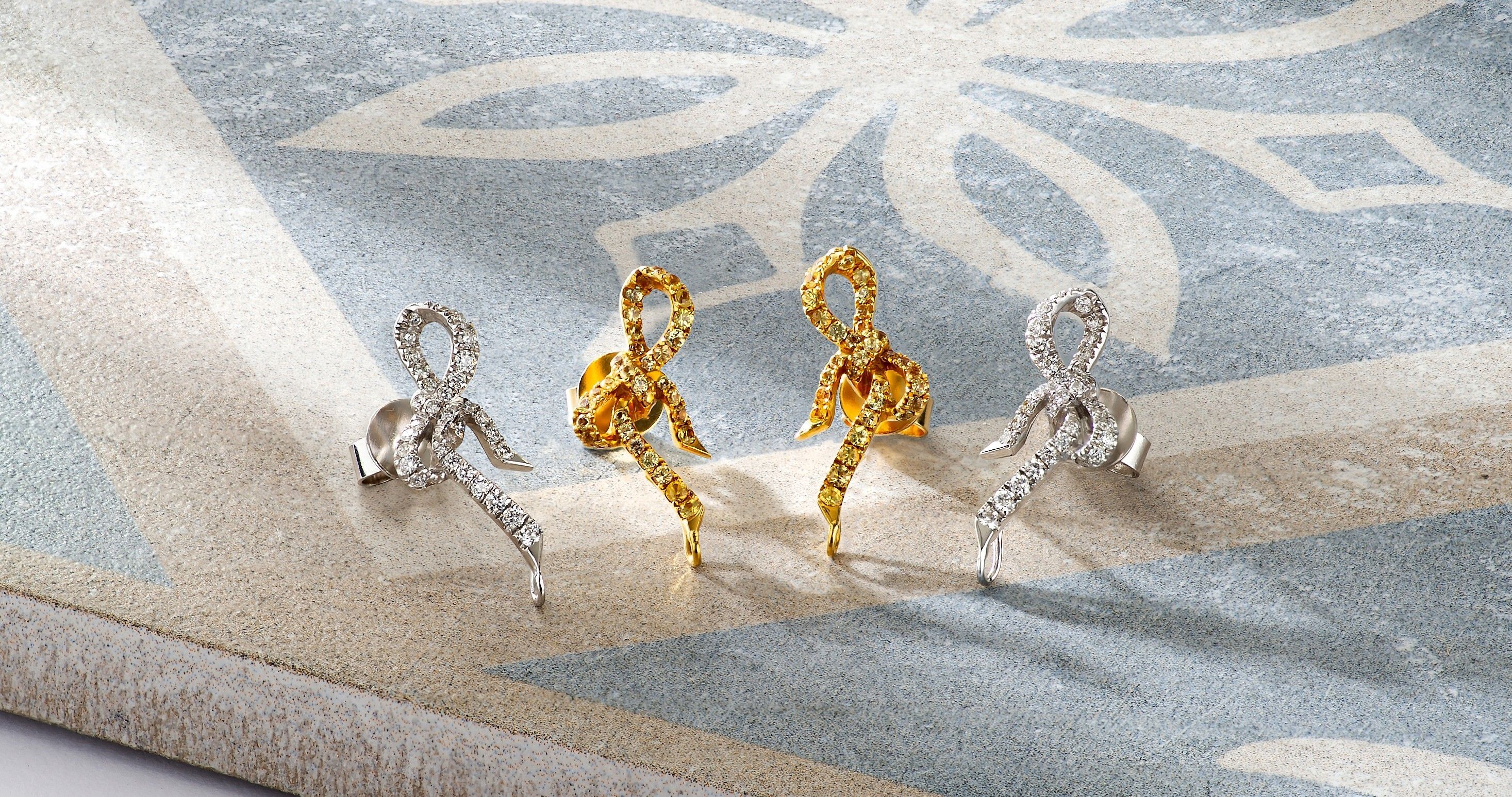 Two pair of delicate 18K gold diamond bow-shaped earrings.