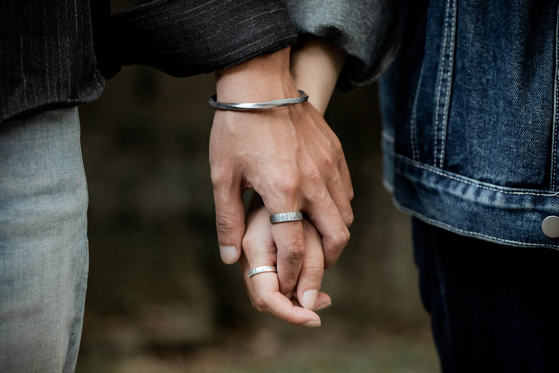 情侶牽手實戴照,男款配鍛敲莫比烏斯純銀手環與鍛敲歲月寬版戒,女款配戴鍛敲莫比烏斯手環與鍛敲歲月細戒,戶外自然光