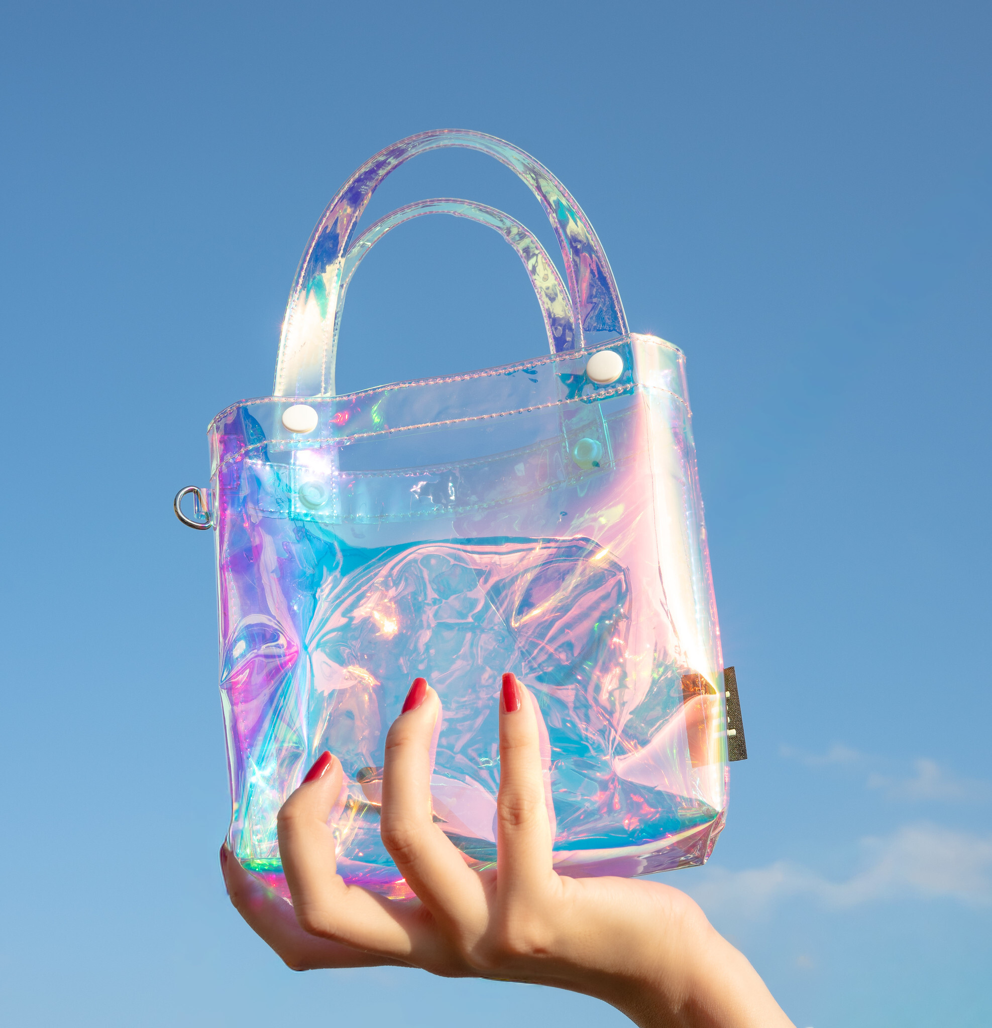小小PETIT 小小微光包｜手拎透明虹光PVC托特包在藍天下拍攝，呈現彩虹折射質感與時尚光澤，手模展示包款細節
