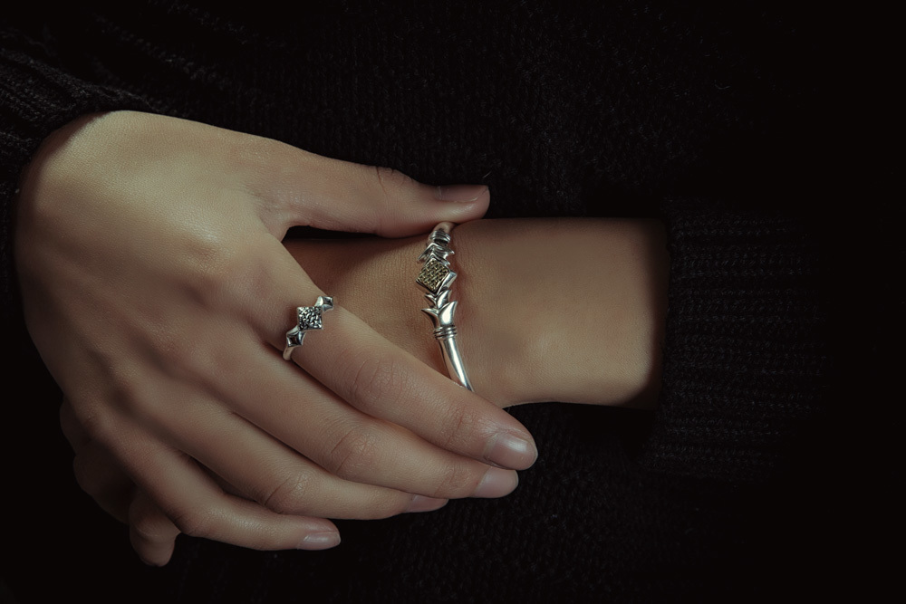 雙手交疊的近拍,指間佩戴山紋甲純銀戒指,手腕配同系列山紋甲手環,深色衣著營造沈穩風格