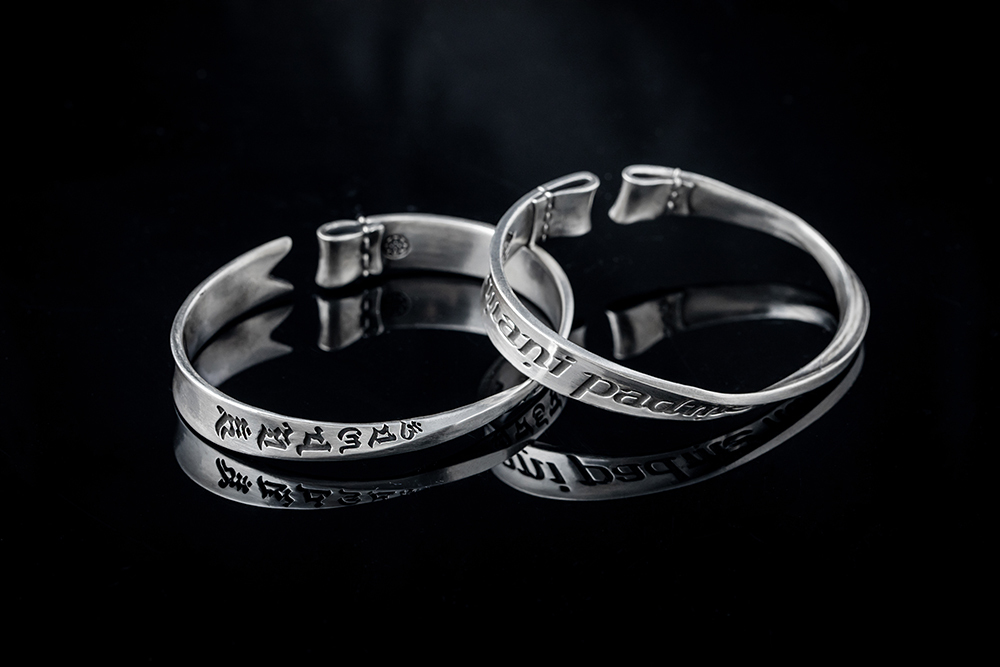 925純銀六字真言手環商品照,扁平帶身刻有真言與願旗字樣,黑色背景反射金屬質感