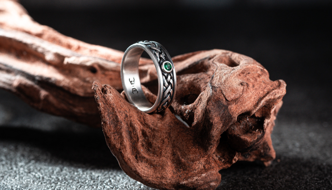 交錯編織紋的【交錯之境 純銀戒指】商品照,鑲嵌深綠鋯石,置於原木質地道具上呈現立體層次