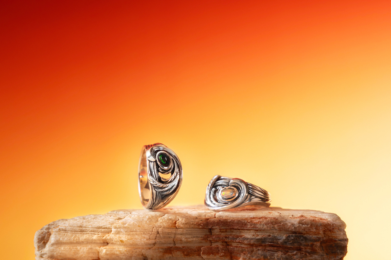 翎火・聖燄戒指商品照,展示純銀羽翼火焰造型與綠色、白色蛋白石戒面,在暖橘背景下呈現立體紋理細節的設計戒指。