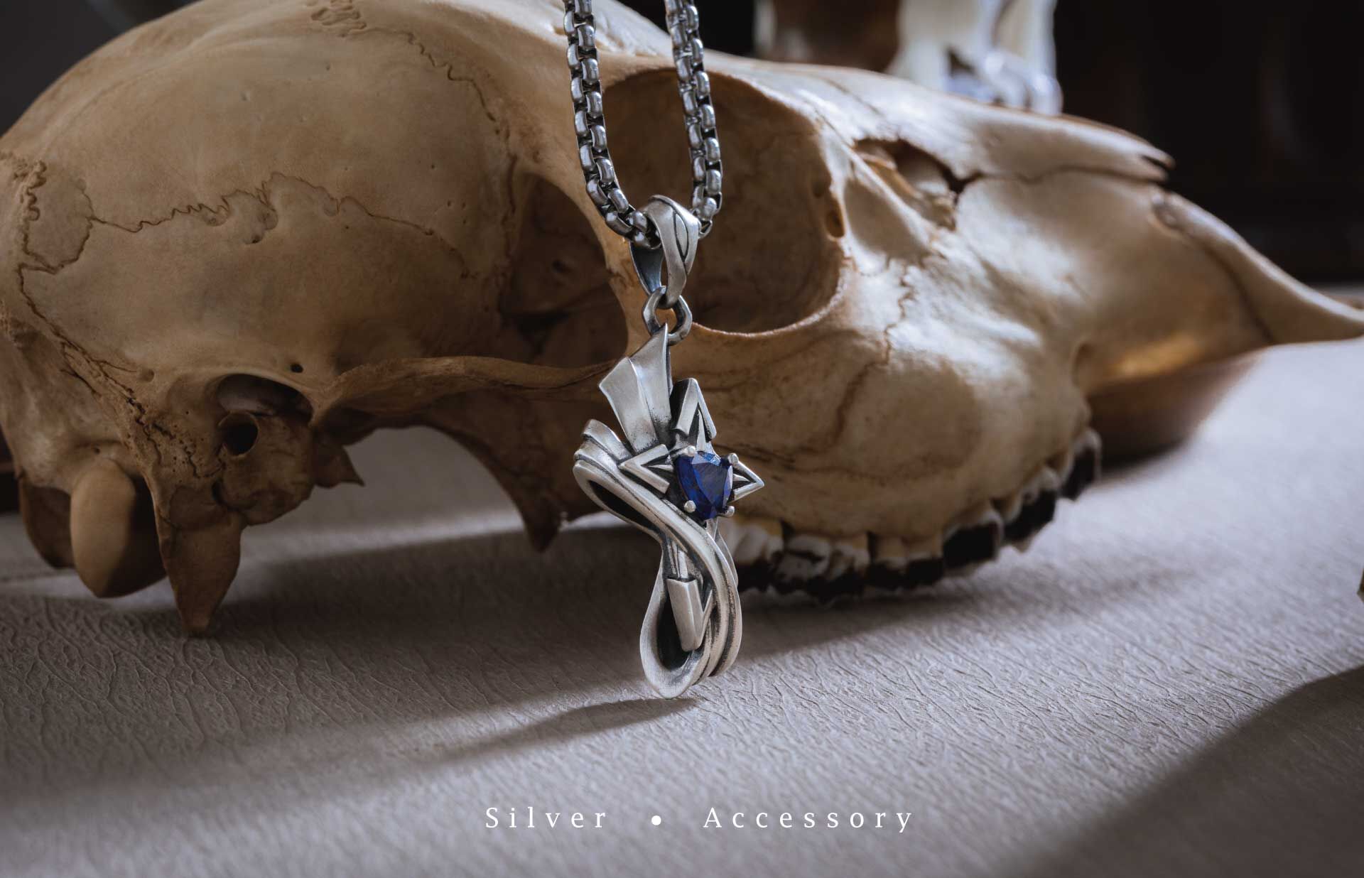 南十字星純銀吊墜商品照,呈現藍色鋯石與十字星造型的立體雕紋細節,於骸骨背景前展現神秘與力量感的銀飾設計。