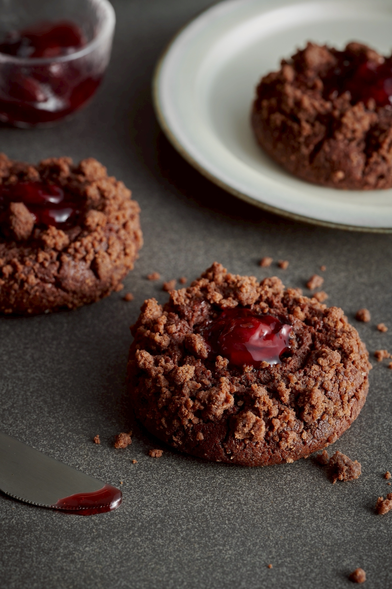 Close-up of a Black Forest soft cookie topped with chocolate crumble and filled with black cherry compote, placed on a dark tabletop.