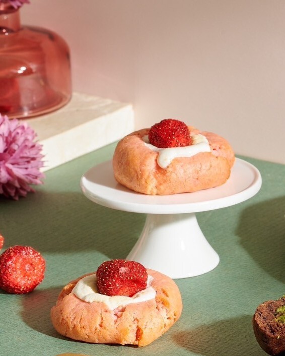 Strawberry Marshmallow Soft Cookies displayed on a white mini cake stand and tabletop, featuring pink cookie dough, marshmallow filling, and a whole strawberry under soft lighting.