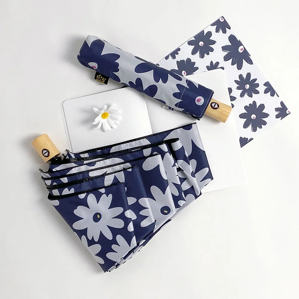 一把藍底白色花朵圖案的自動傘及一把白底藍花圖案的自動傘平放在白色背景上,旁邊放著一朵雛菊裝飾。