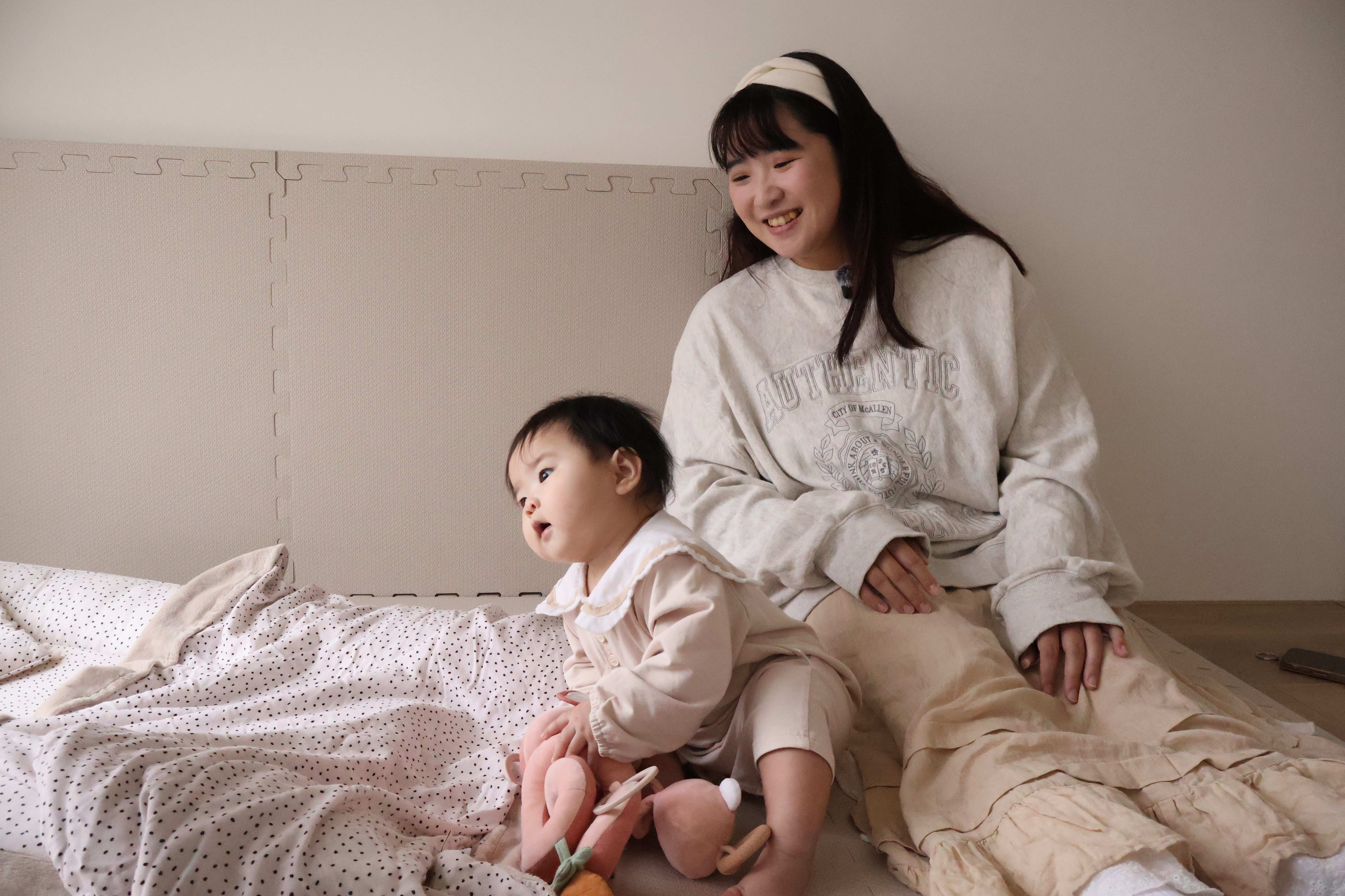 Nao媽媽與朵朵在米蘭暖陽睡窩上的親子互動，寶寶手持安撫玩具，歪頭看向窗外風景。