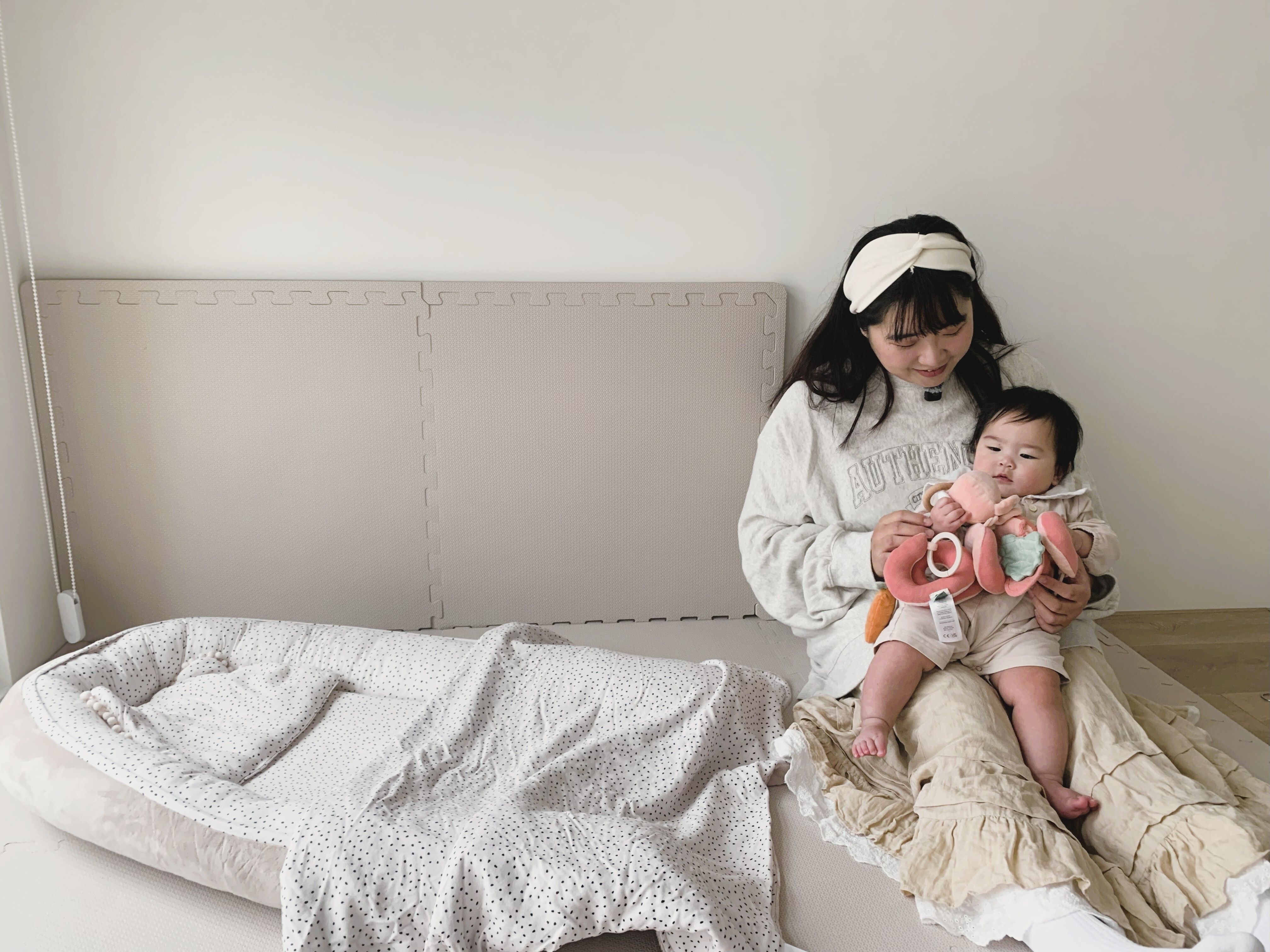 Nao媽媽抱著朵朵與米蘭暖陽睡窩合照，寶寶手持Trixie動物造型捲捲安撫玩具的可愛畫面。