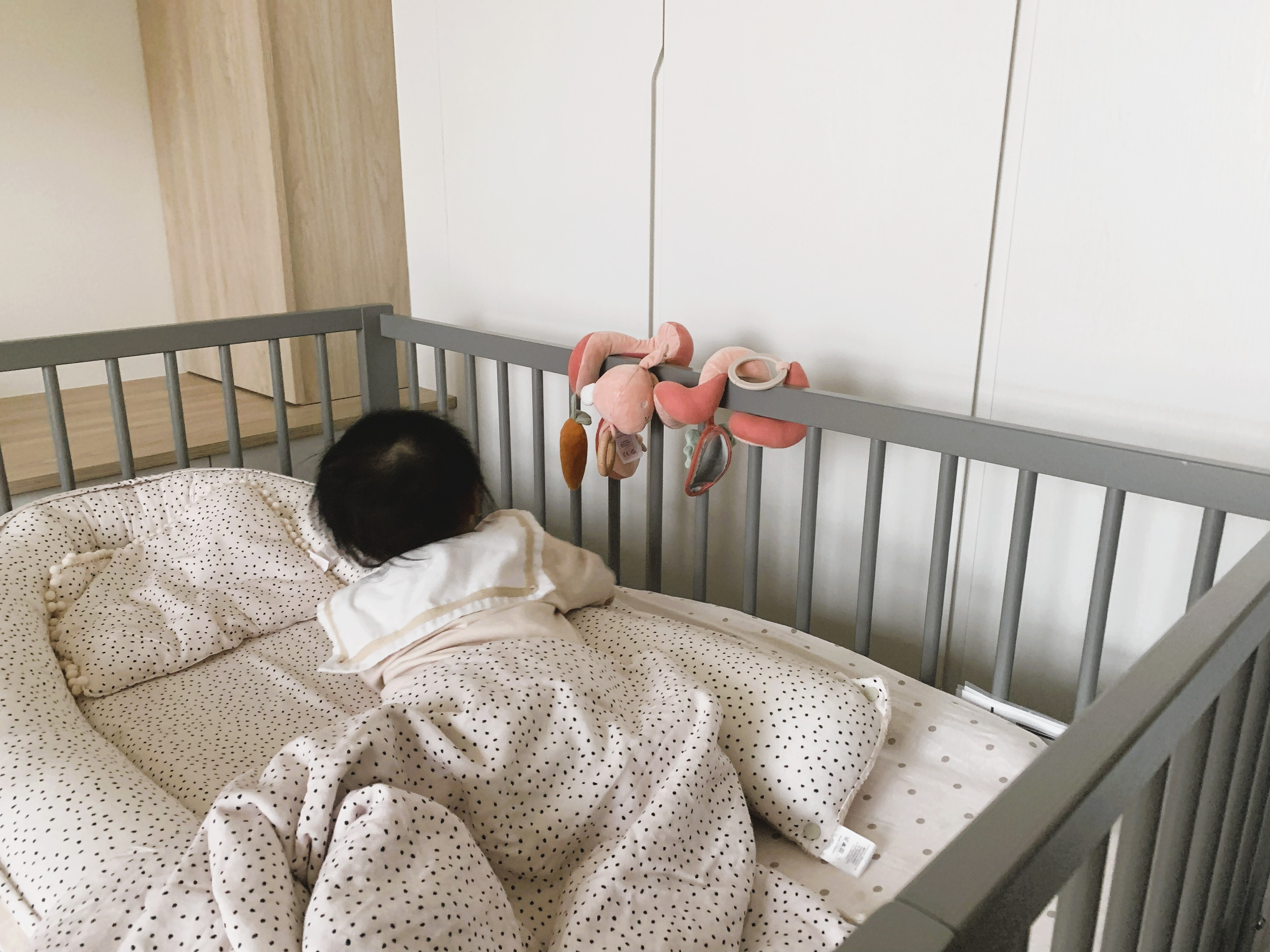 寶寶在嬰兒床中，搭配米蘭暖陽睡窩與兔子造型安撫玩具，展現莫蘭迪色系嬰兒房佈置風格。