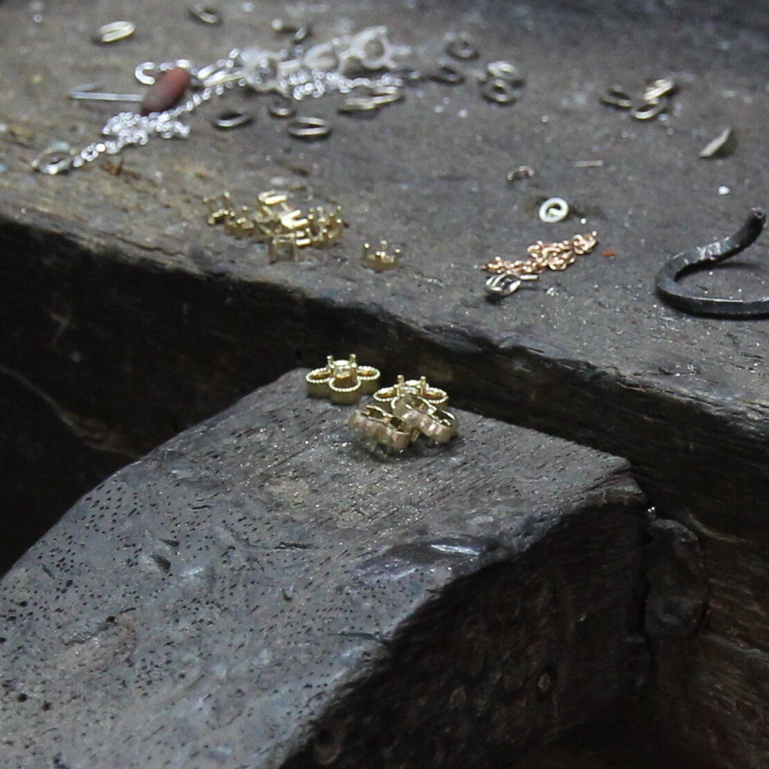 Gold ring settings and scattered jewelry components on a worn jeweler’s workbench.