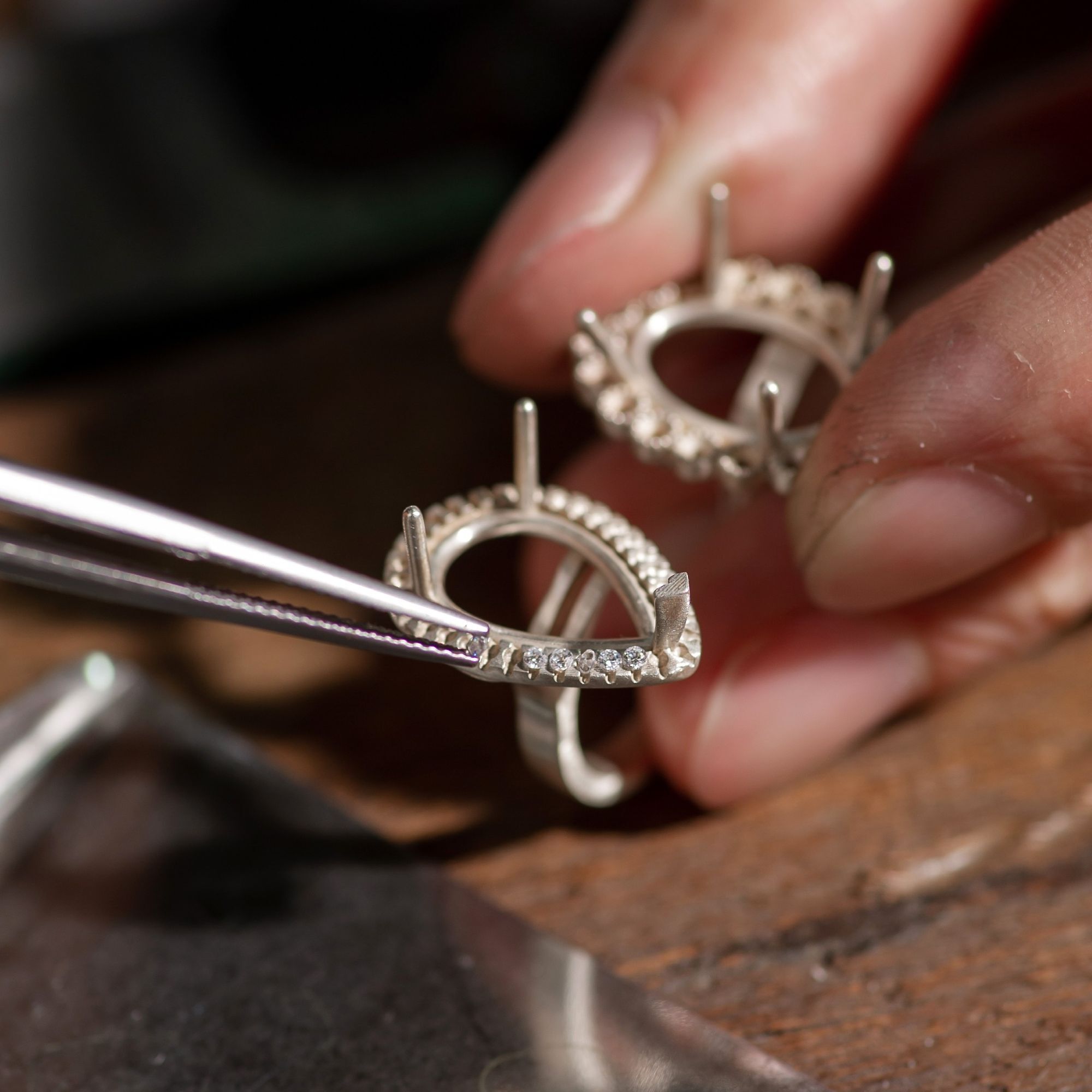 A jeweler setting small diamonds into a ring mounting using precision tweezers.