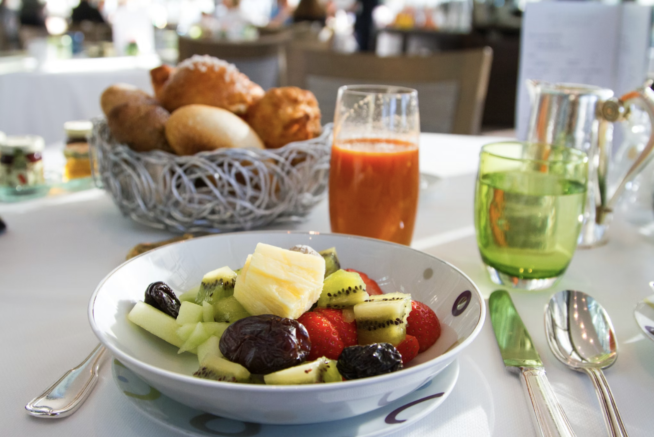 白色桌布上的早餐桌景,水果沙拉、麵包籃與多杯果汁,呈現悠閒豐盛的用餐氛圍