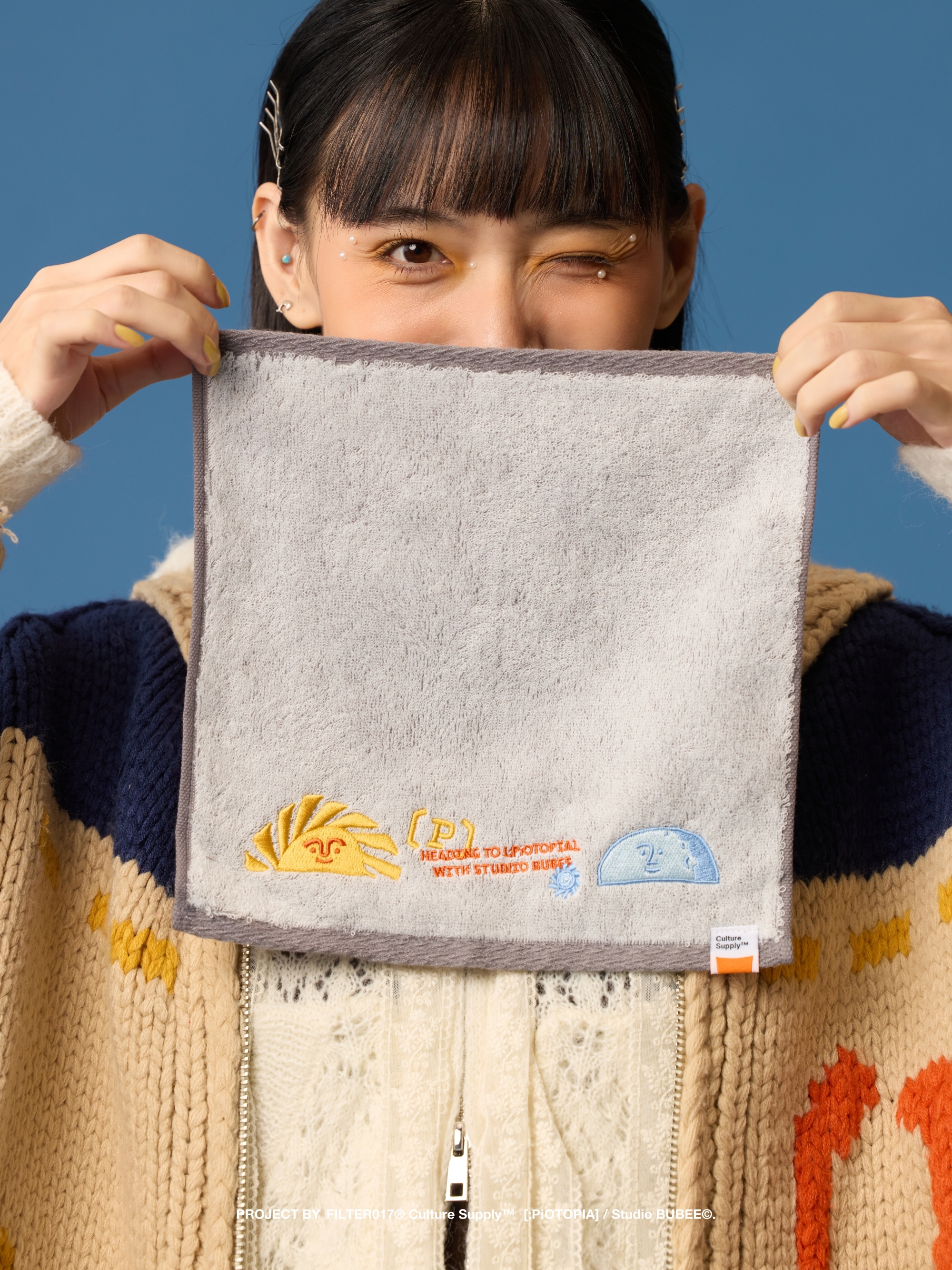 女孩雙手拿著手拿灰色刺繡毛巾，上面刺有太陽及月亮圖案