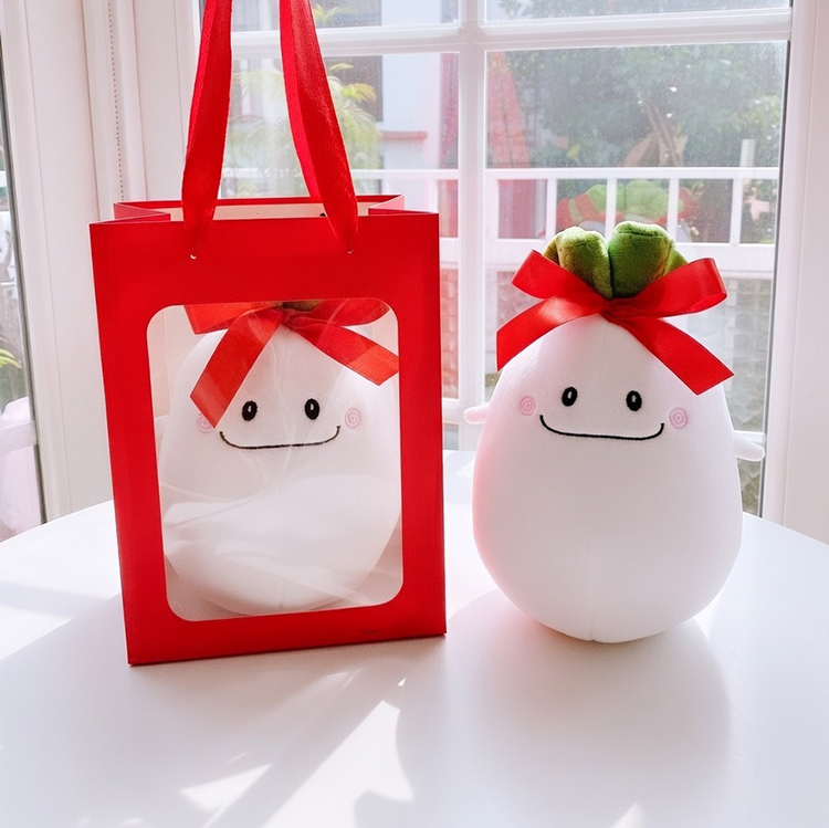 桌上的白蘿蔔好彩頭玩偶與紅色透明視窗禮物袋