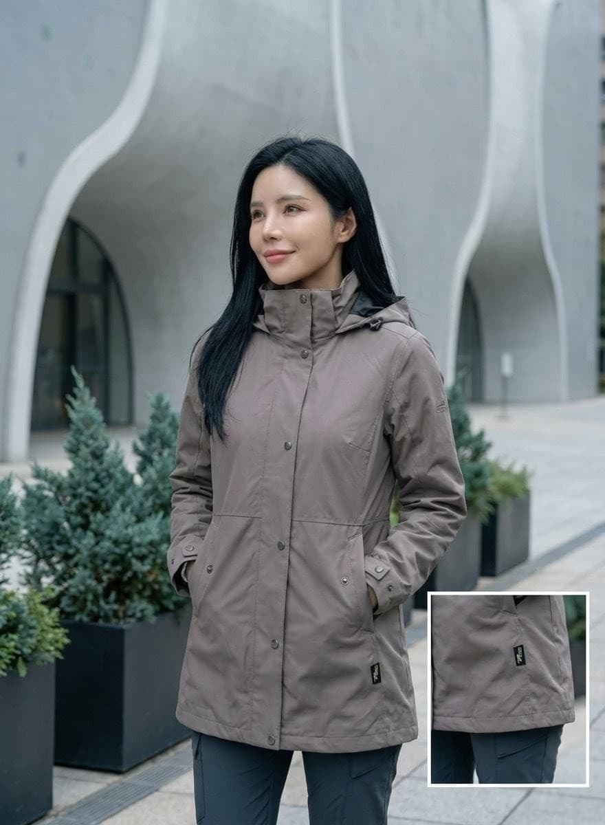 女防風保暖外套人物： LÄCHELN 專屬繆思（174cm、小 V 臉、黑色長直髮、自信微笑）。 穿著： 穿著 L34W505 灰褐色外套，內搭簡單的冷調深色長褲，拉鍊半開露出輕盈感。 環境： 台中國家歌劇院旁的清水模建築景觀，背景帶有淡淡的冷杉綠植栽。 氛圍： 低飽和度、大地色系基底、靜謐的都會機能感 (Urban Outdoor Calmness)。 特寫： 外套下擺落在大腿處的 83 公分長度特寫，展現布料細緻的壓紋與專業標章。