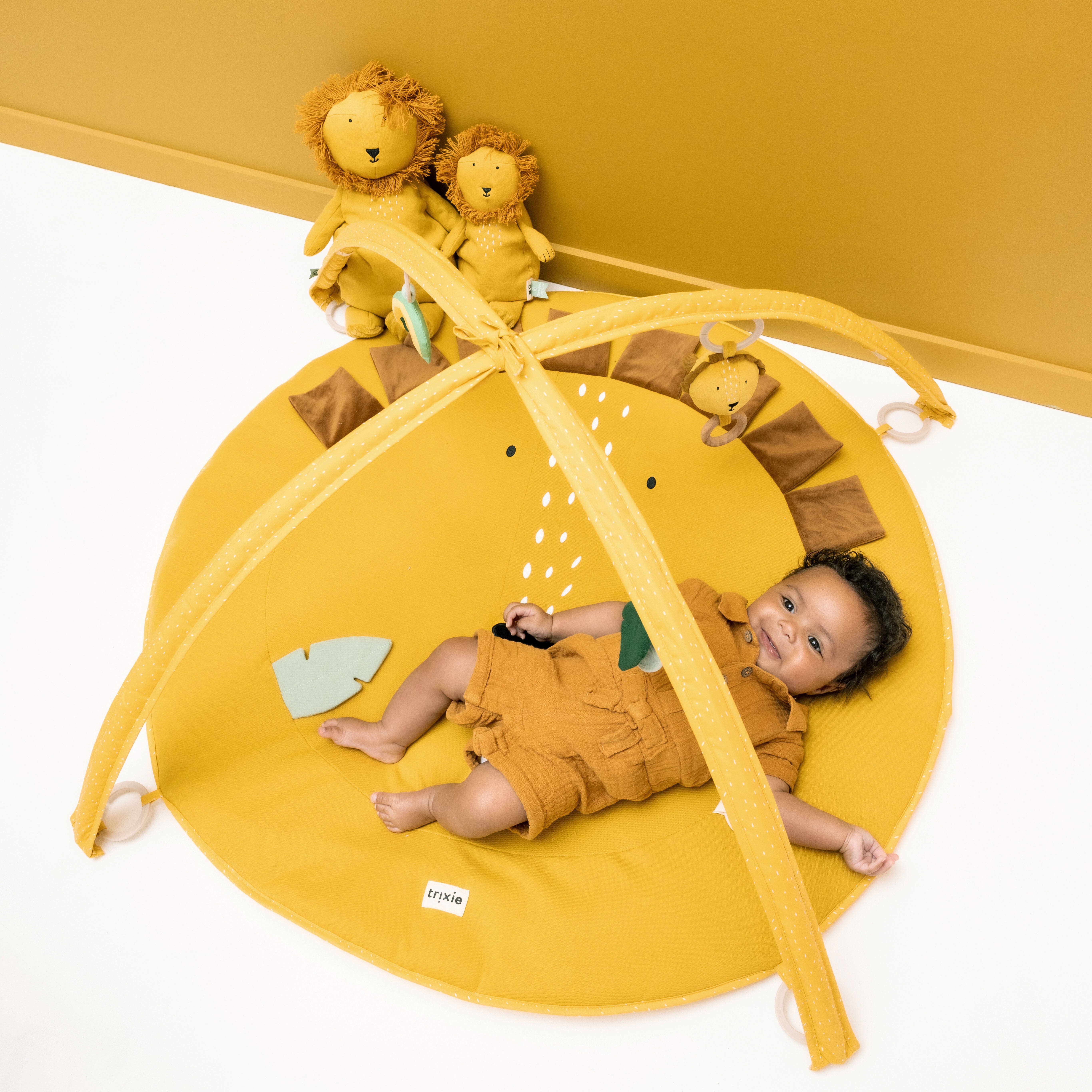 寶寶躺在黃色獅子造型的比利時 Trixie 動物造型感統遊戲墊上，進行抬頭訓練與感官探索。