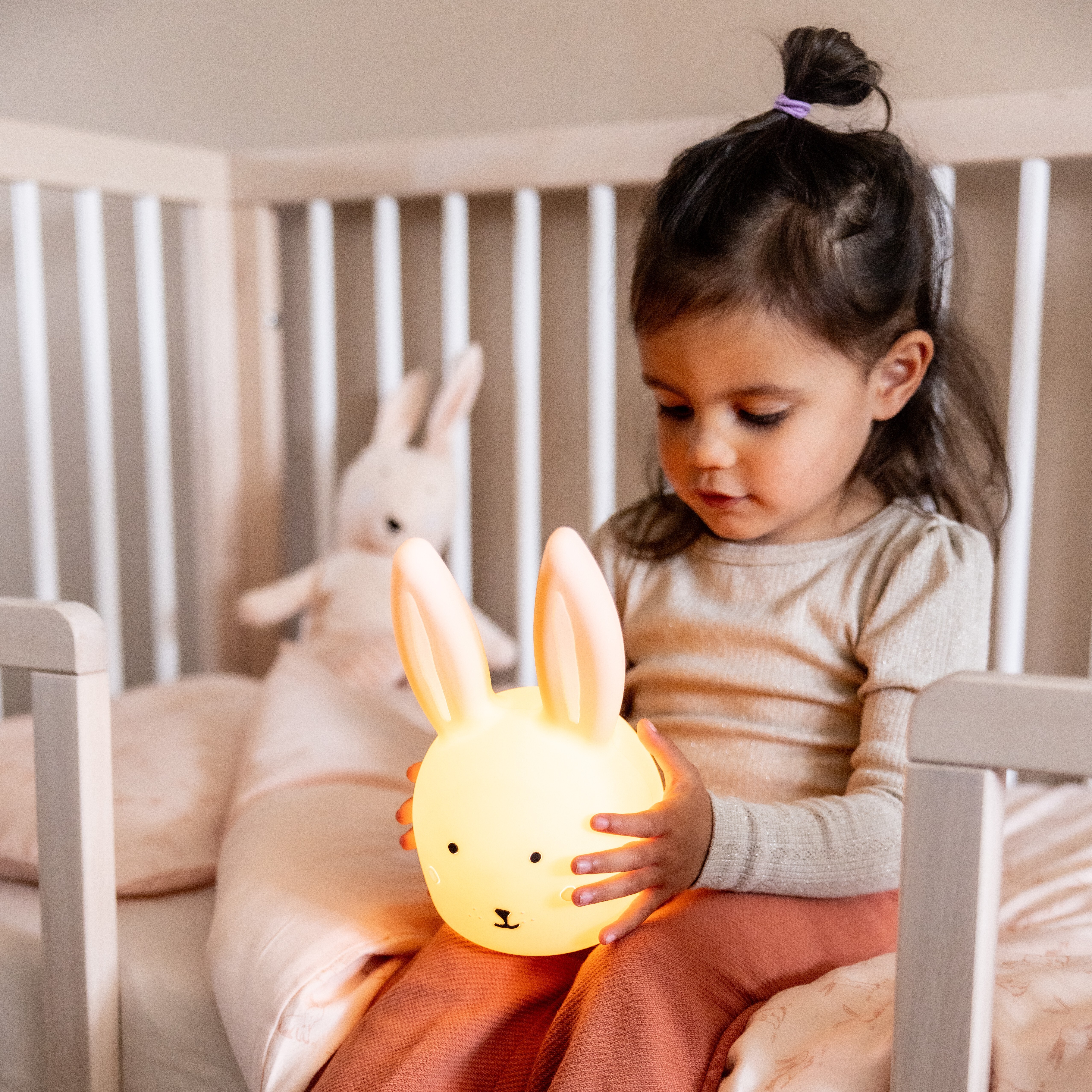 幼兒在床上抱著發光的小兔造型比利時Trixie矽膠夜燈，燈光溫暖柔和。