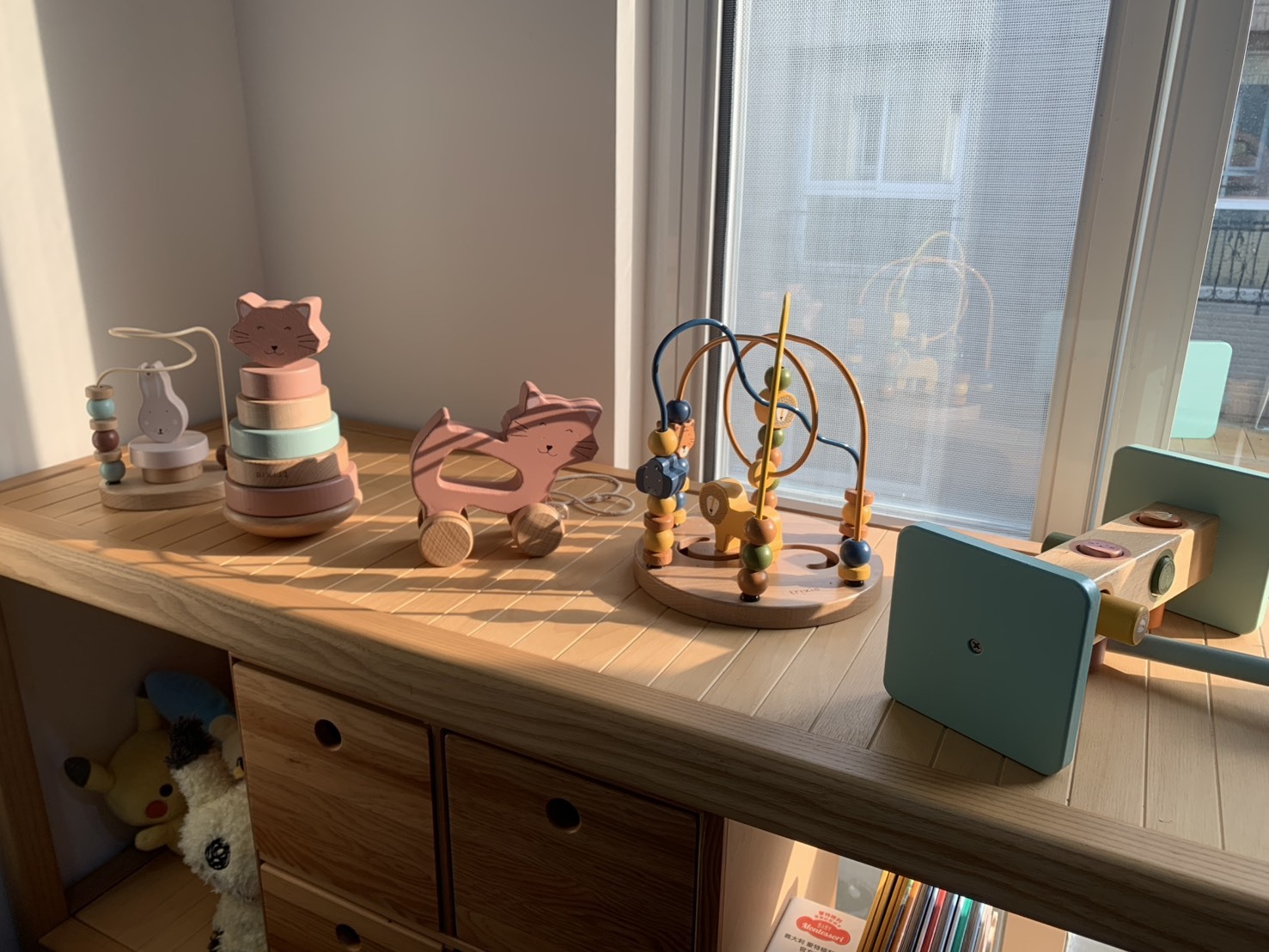 陽光灑在木質收納櫃上的巴黎香頌木玩系列，包含撥珠台、疊疊樂、拉車。