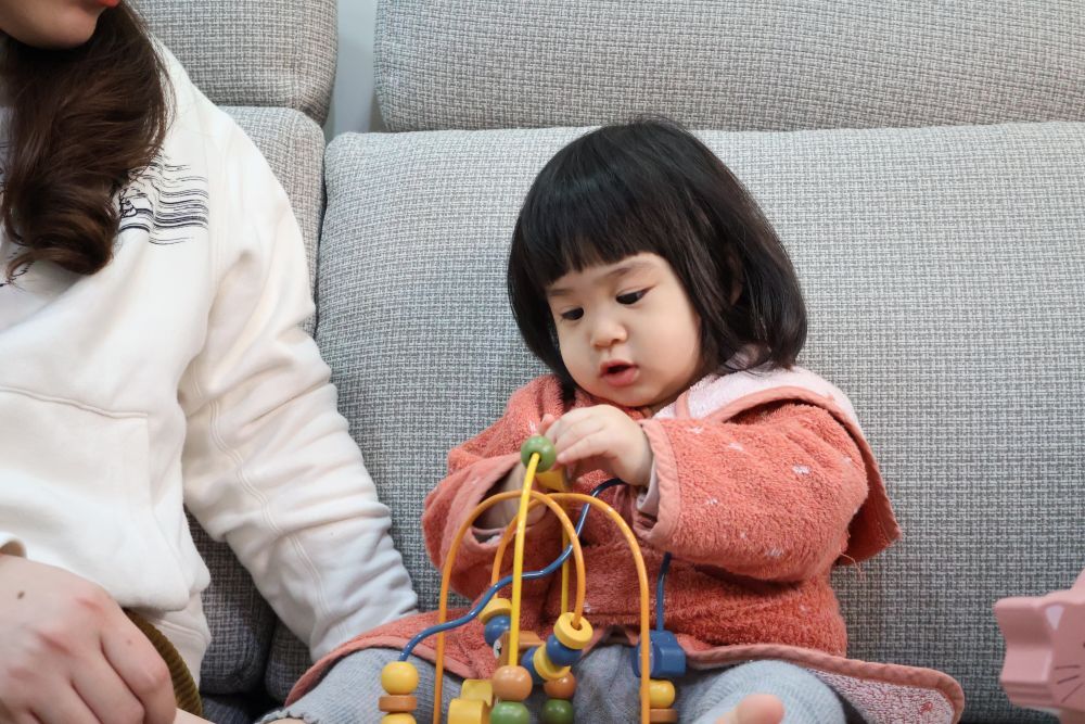 一歲半的小梅子專注地玩著 Trixie 木玩趣味撥珠台，練習手指撥動彩色木珠。