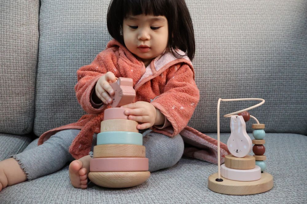 小梅子坐在沙發上玩 Trixie 動物造型木玩疊疊樂，旁邊放著兔子造型撥珠台。