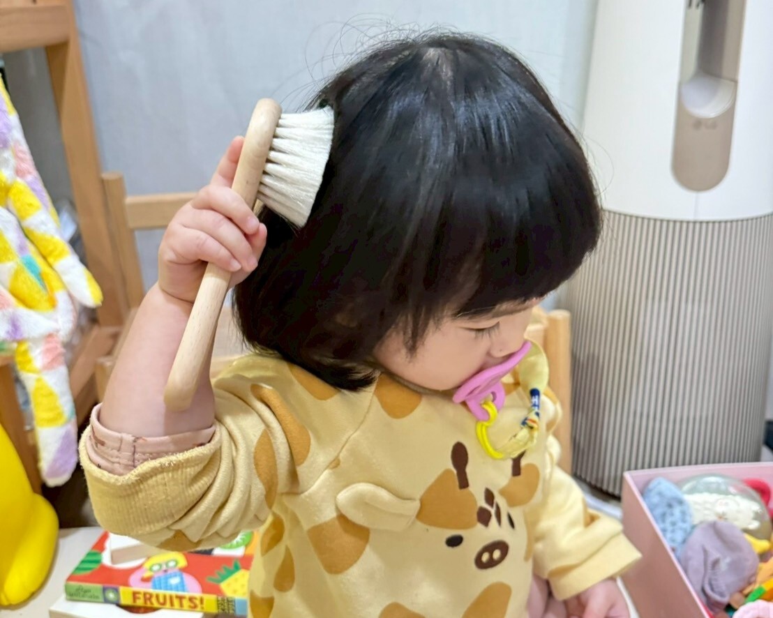 小梅子自己拿著 Maylily 羊毛梳嘗試梳理頭髮，練習生活自理與觸覺感受。
