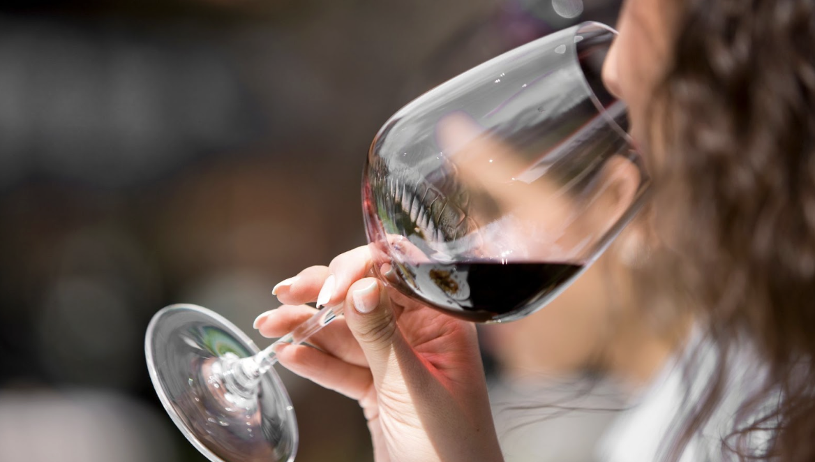 一名女子正舉起透明高腳杯飲用紅酒的側臉特寫,展現社交場合或品酒的悠閒氛圍。