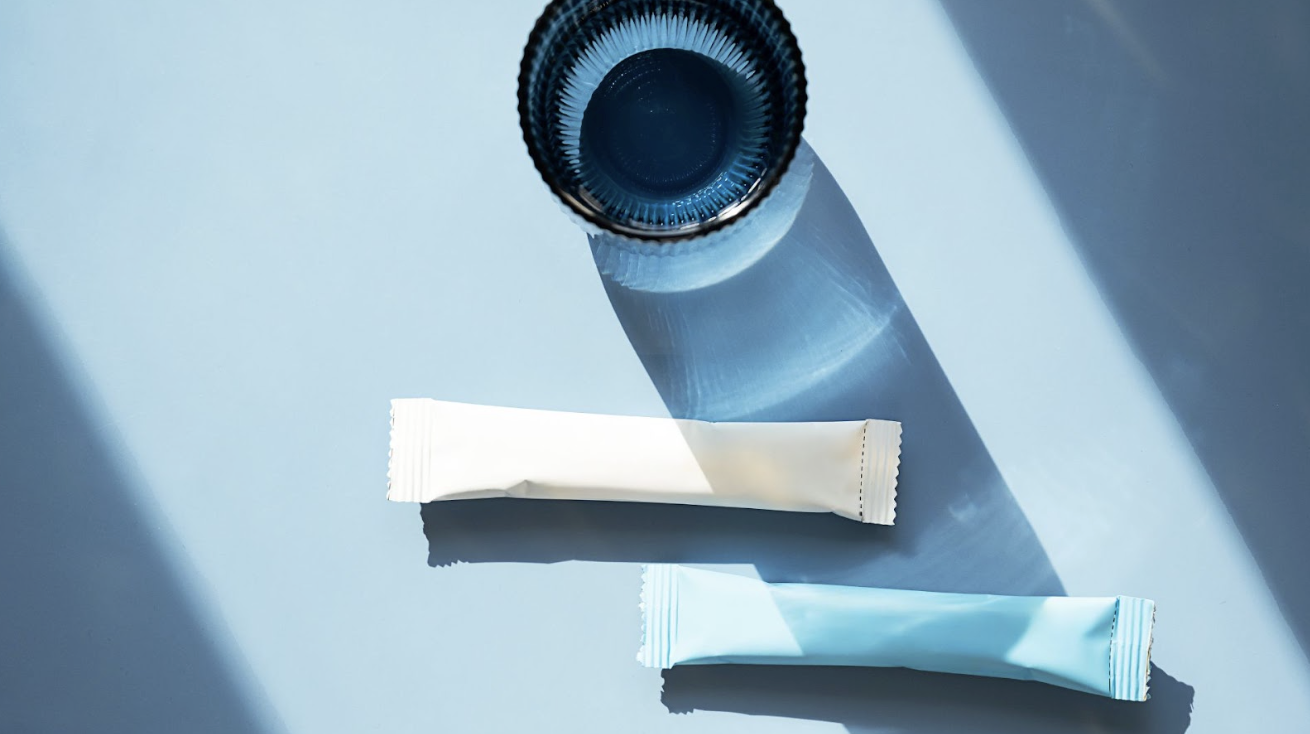 藍色背景下，由上方俯瞰拍攝的一杯藍色水與兩條長條狀隨身包產品，光影投射出簡約清爽的視覺感，適合展示產品便攜性。